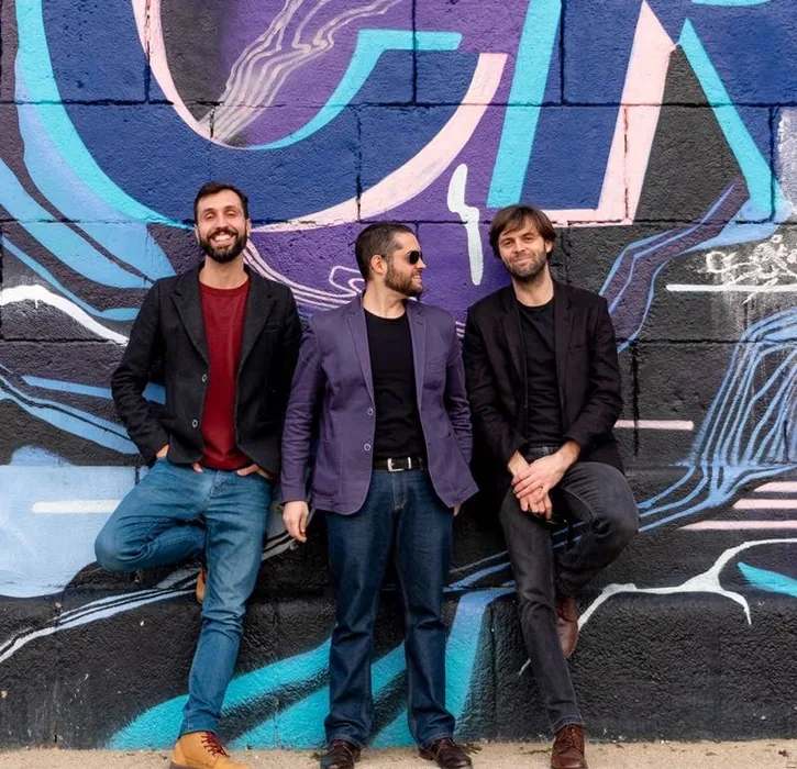 Umberto with his trio in front of a blue and pink painted wall